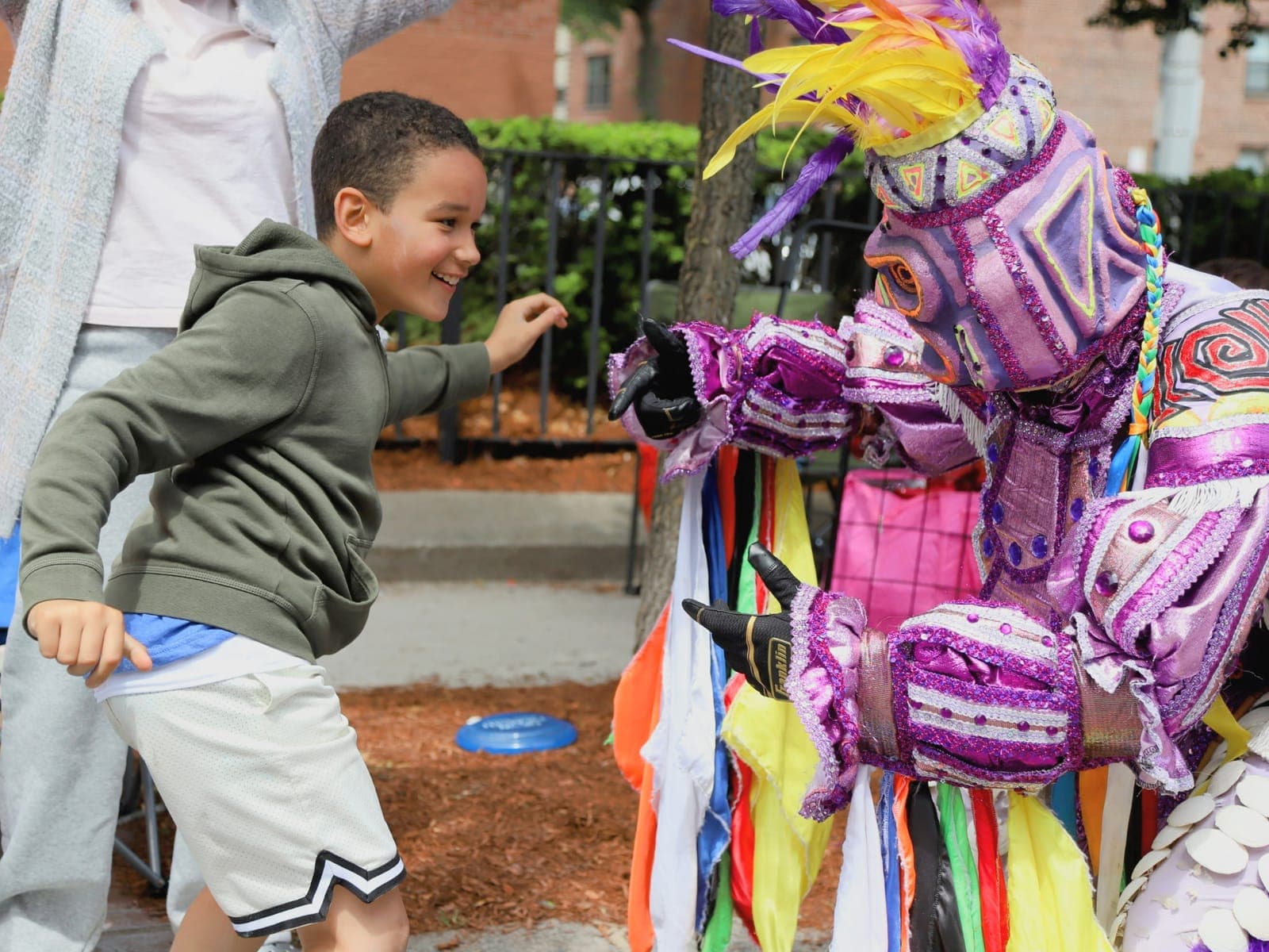 A child smiles and reaches toward an ACM performer in a colorful Dominican Carnaval costume