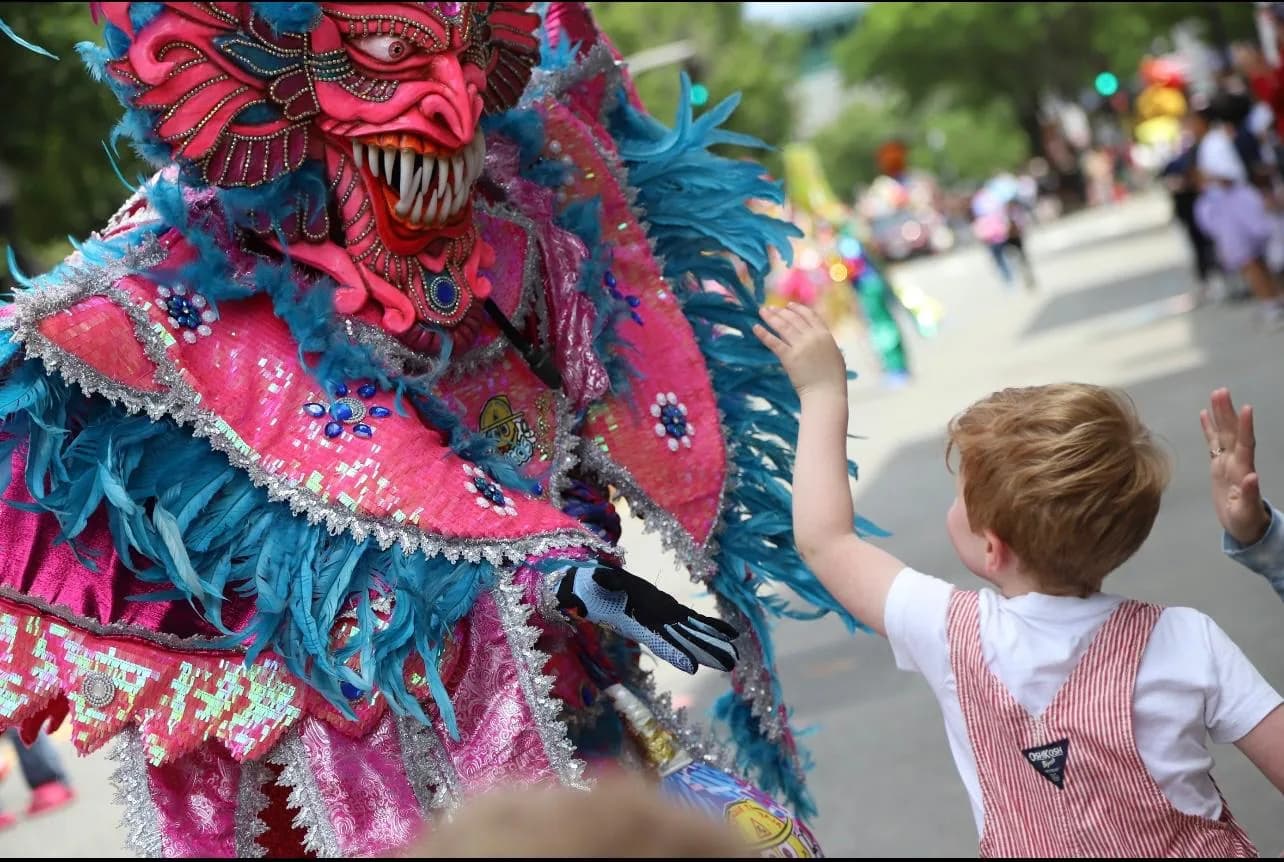 A child shares a high-five with a brightly costumed Dominican Carnaval performer