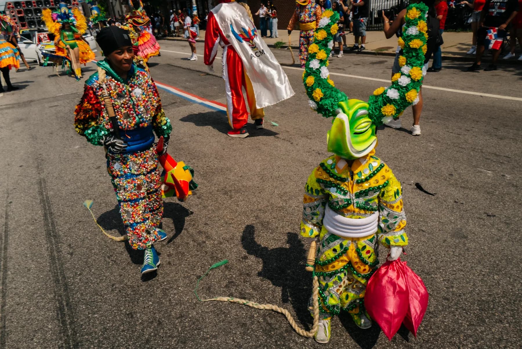 Two ACM performers in green and pink Carnaval costumes advance along the Providence route